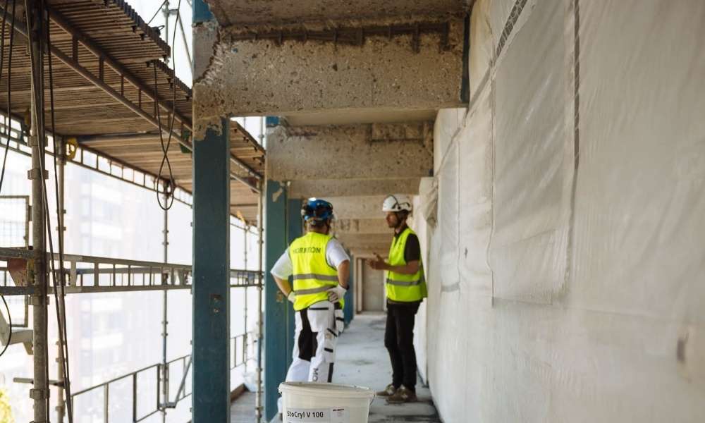 Möte på byggställning där betongskador i fasad bedöms inför val mellan betongreparation och betongrenovering.